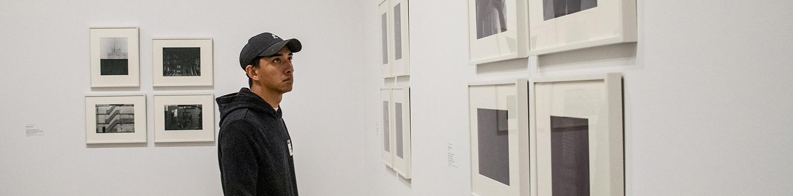 A student intern is looking at a wall of art in a gallery.