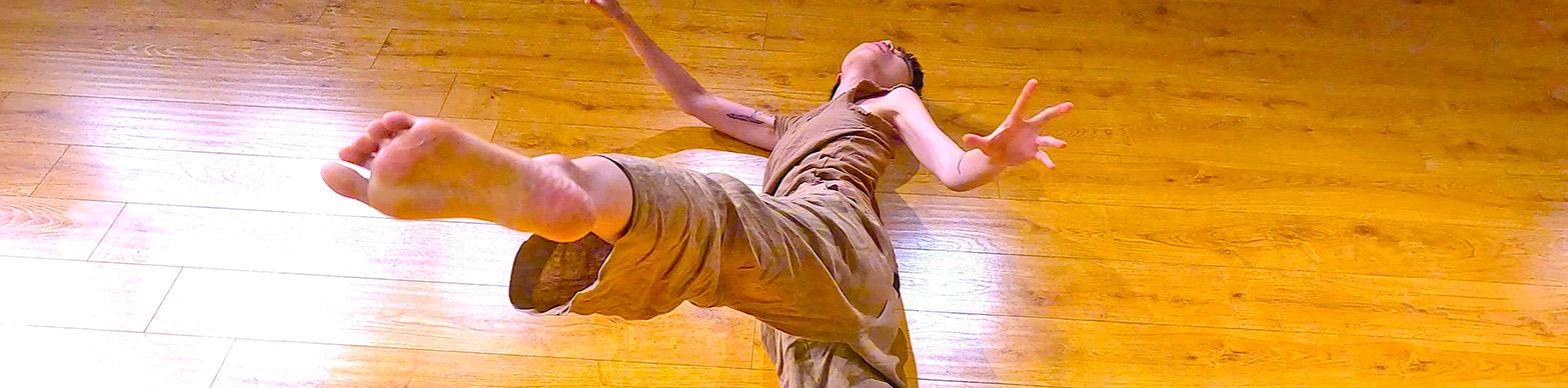 A dancer lays on the floor and kicks their leg up to the camera