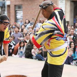 Two japanese men in traditional garb hammering mochi in front of a crowd. 
