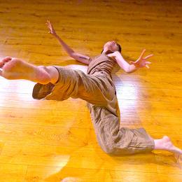 A dancer lays on the floor and kicks their leg up to the camera